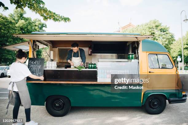 female owner adjusting board on concession stand while partner working in food truck - schürze mann rückansicht stock-fotos und bilder