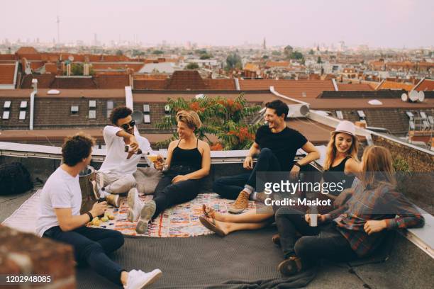 happy friends enjoying beer while sitting at terrace during rooftop party in city - beer friends imagens e fotografias de stock