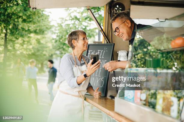 female owner showing smart phone to male coworker while standing by food truck - business couple showing stockfoto's en -beelden