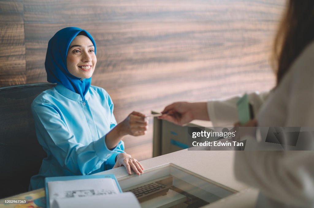Malaysia hospital registration counter asian female receptionist getting payment from the female hijab Muslim patient accepting her credit card