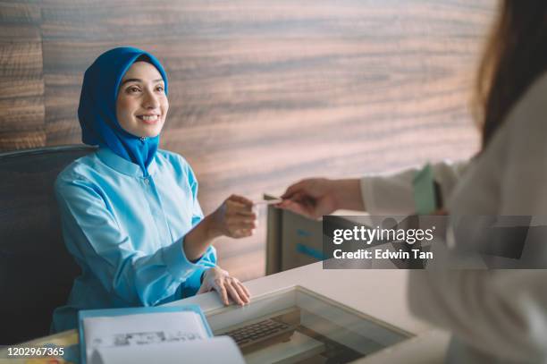 malaysia hospital registration counter asian female receptionist getting payment from the female hijab muslim patient accepting her credit card - asian receptionist stock pictures, royalty-free photos & images