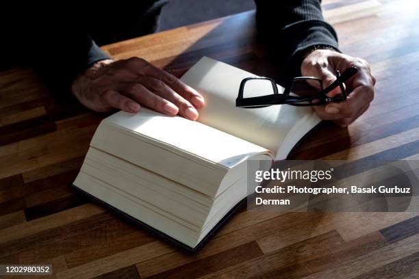 a man holding reading glasses and reading a book - thick reading glasses stock pictures, royalty-free photos & images