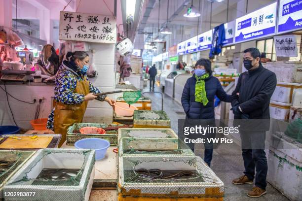 Shanghai, China, 26th Jan 2020, Woman store vendor wearing masks shows living eel to couple wearing masks at seafood market.