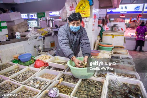 Shanghai, China, 26th Jan 2020, A store vendor wearing a masks handles shellfish with hands at seafood market.