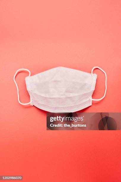 still life of a white face mask on red background - griepmasker stockfoto's en -beelden