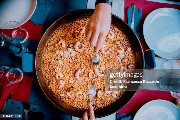 hands of a couple sharing traditional paella de mariscos - dining overlooking water stock-fotos und bilder