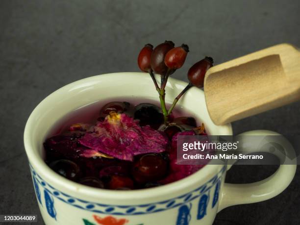 a cup with dish of hot infusion of medicinal herbs with rose hips, hawthorn and rose petals and a wooden shovel - hot hips 個照片及圖片檔