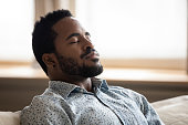 Tranquil young african man resting eyes closed breathing on couch