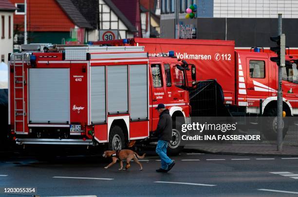 Man with a dog walks past fire-fighting vehicles at the site where a man who drove into a carnival procession, on February 25, 2020 in Volkmarsen...