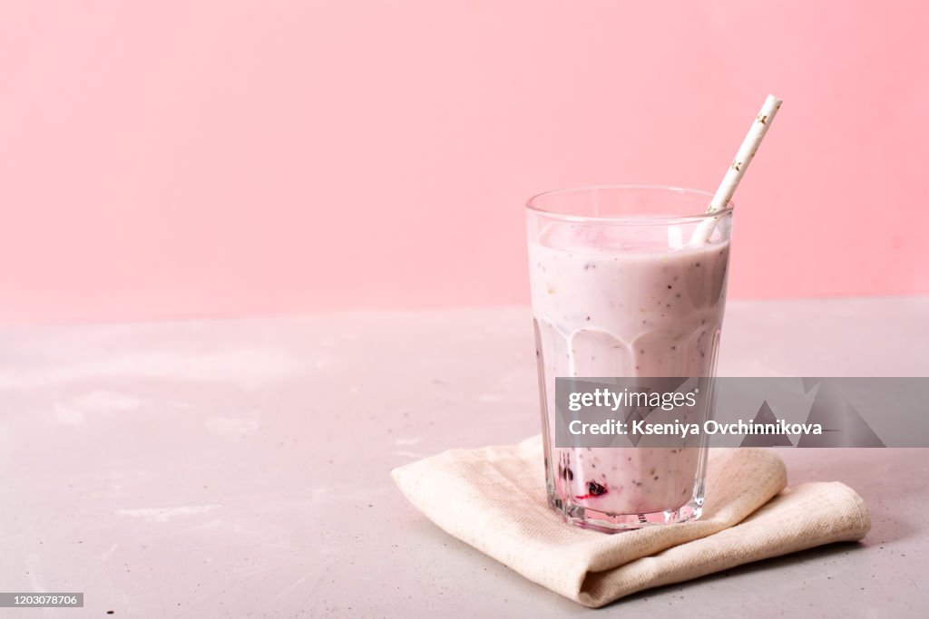 Two glasses of blueberries smoothie on pink background. Poring from blender into glass.