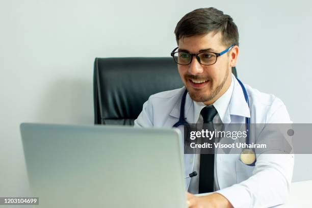 doctor working with laptop computer at his desk in his office. - gp practice stock pictures, royalty-free photos & images