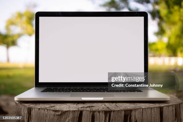 laptop with blank white screen on wood stump against nature background - computer mockup foto e immagini stock