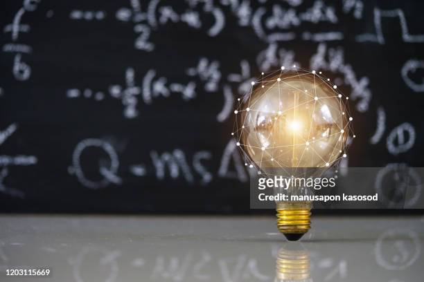 hand holding light bulb on blackboard background. - halogen light stock pictures, royalty-free photos & images