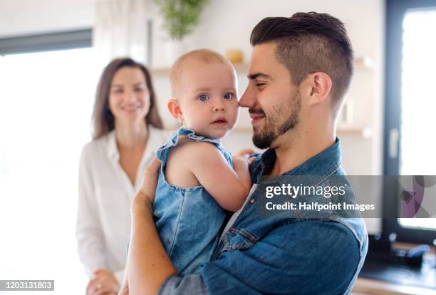 portrait of young couple with toddler girl indoors in kitchen at home. - baby blue stock pictures, royalty-free photos & images