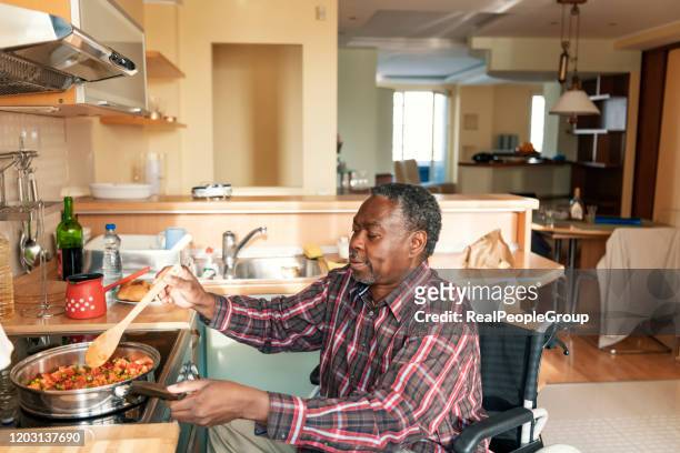 l'afro-americano senior in sedia a rotelle sta preparando un pranzo a casa - accessibilità foto e immagini stock