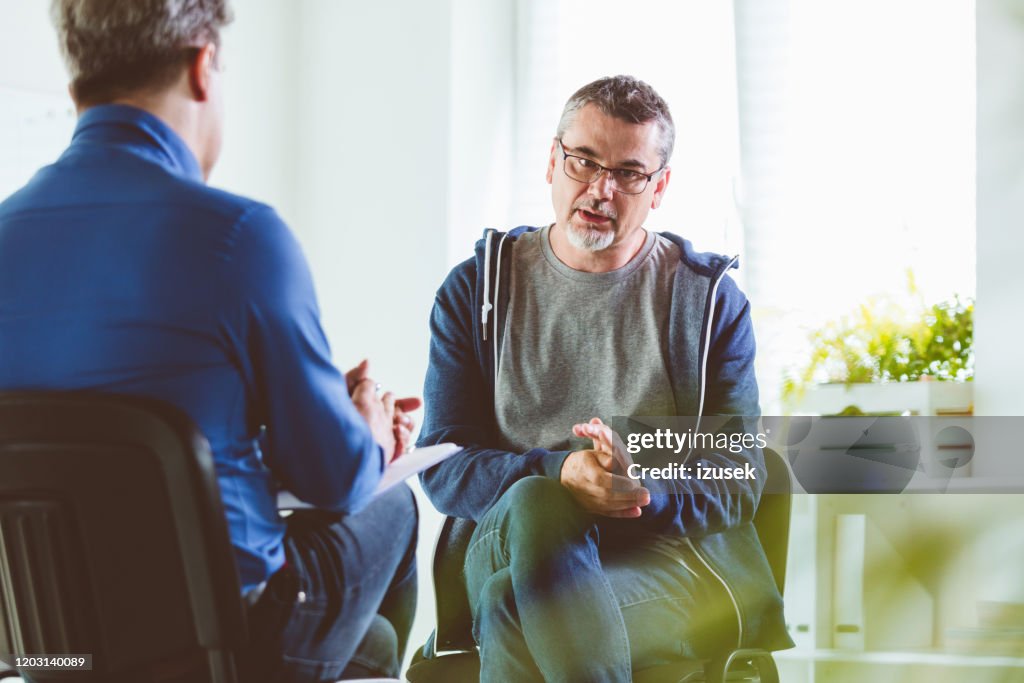 Reifer Mann im Gespräch mit Psychotherapeuten in seinem Büro