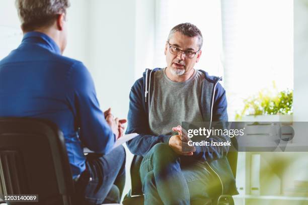 rijpe mens die met psychotherapeut in zijn bureau spreekt - two doctors talking stockfoto's en -beelden