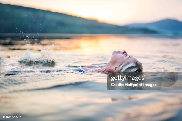 active senior woman swimming  in lake outdoors in nature. copy space. - backstroke fotografías e imágenes de stock