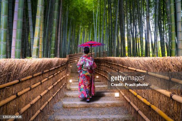 asian young woman traveller wearing japanese traditional kimono with red umbrella sightseeing at famous destination bamboo forest in arashiyama, kyoto, japan. japan tourism, history building, or tradition culture and travel concept - season in kyoto imagens e fotografias de stock