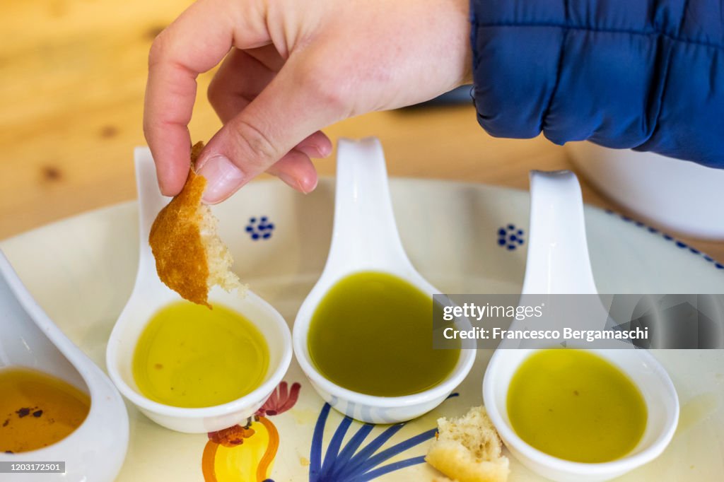 A human hand dips bread in different types of flavored extra virgin olive oils from Apulia, Italy.