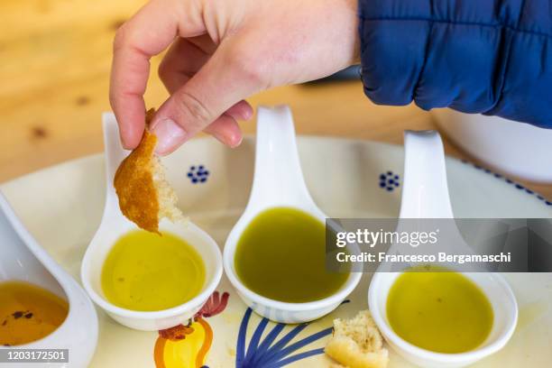 a human hand dips bread in different types of flavored extra virgin olive oils from apulia, italy. - extra virgin olive oil stock pictures, royalty-free photos & images