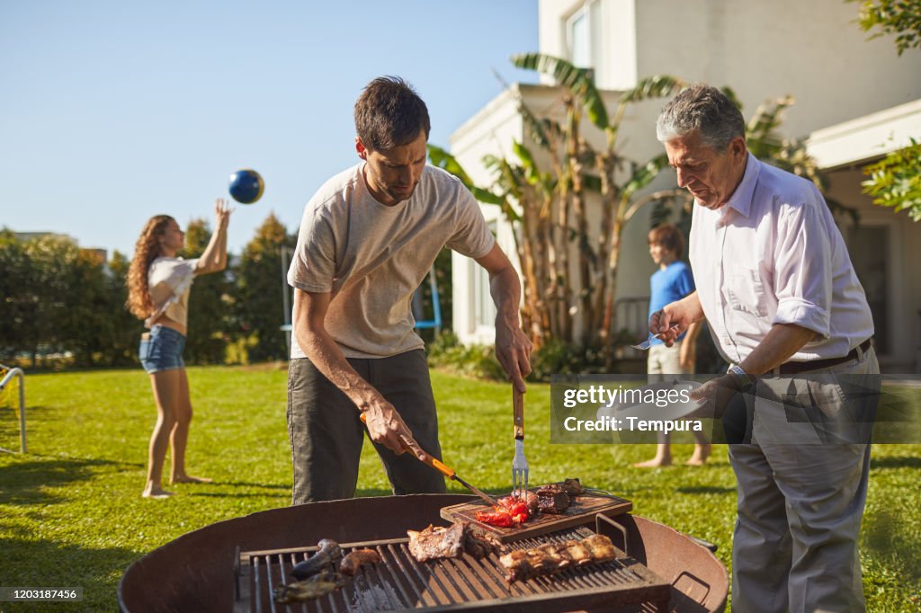 Mid adult son is serving barbecued meat to his senior father.