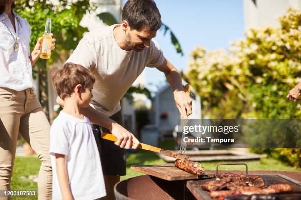 vater grillt fleisch mit seinem sohn im garten. - bbq father stock-fotos und bilder