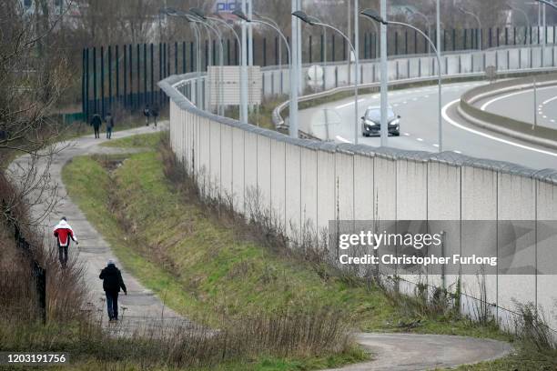 Migrants walk along the security wall protecting the Rocade, Calais Ferry port’s main dual-carriageway approach, on January 31, 2020 in Calais,...