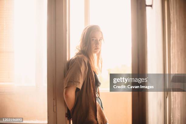 young woman leaning on balcony doorway at home in summer - woman standing in doorway stock pictures, royalty-free photos & images