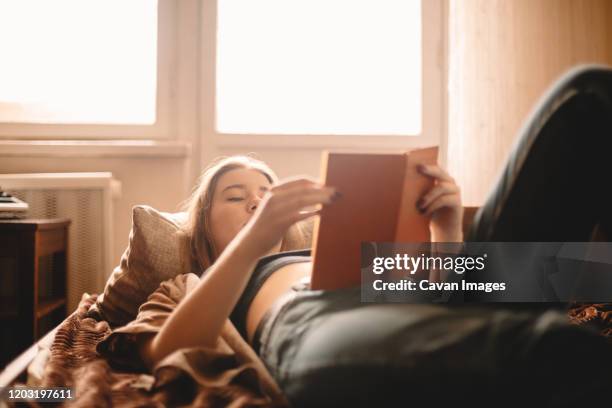 teenage girl reading book while lying on bed at home - bed sun stock pictures, royalty-free photos & images