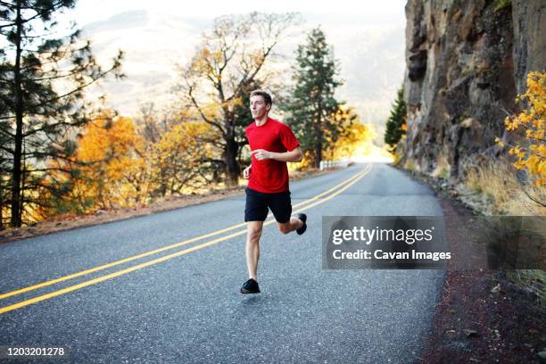 male runner in his mid 20s running along scenic road in rowena - striding stock pictures, royalty-free photos & images