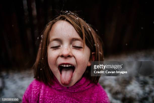 young girl trying to catch snow flakes on her tongue in winter - face sommersprossen stock-fotos und bilder