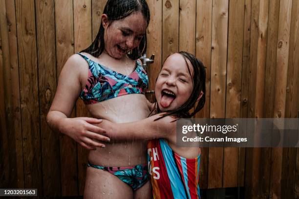 sisters playing in outdoor shower on a summer day - oberkörper happy sommersprossen stock-fotos und bilder