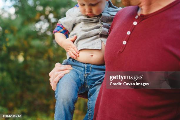 close-up of a toddler in father's arms investigating his exposed belly - fat toddler stock pictures, royalty-free photos & images