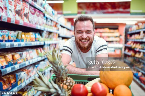 schöne lächelnde male und sein wagen voller supermarkt-produkte - full stock-fotos und bilder