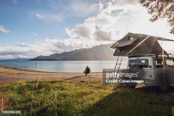 a woman sits along a lake next to a suv with a tent in new zealand - wilderness camping stock pictures, royalty-free photos & images
