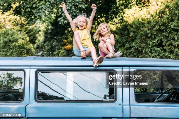 two girls happy and excited sitting on top of vintage car - family shoes stockfoto's en -beelden