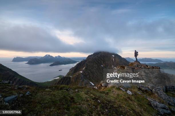 female hiker overlooks moutain landscape from middagstind, flakstady, lofoten islands, norway - bewolkt stockfoto's en -beelden