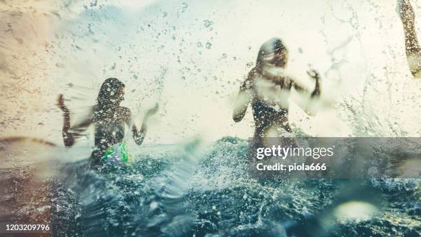 amici che giocano insieme in mare, spruzzando e immergendosi durante un tramonto estivo - acqua splash foto e immagini stock