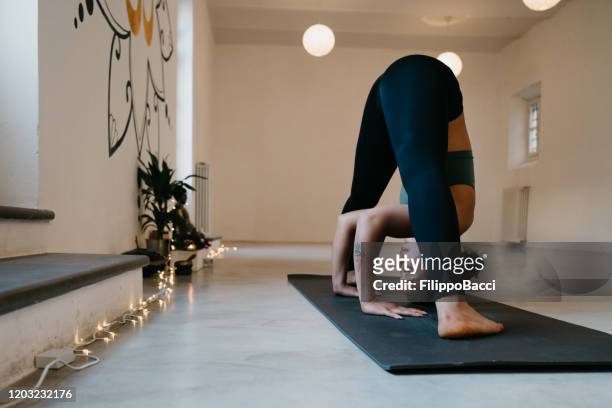 young adult woman practicing yoga in wide-legged forward bend pose - bent stock pictures, royalty-free photos & images
