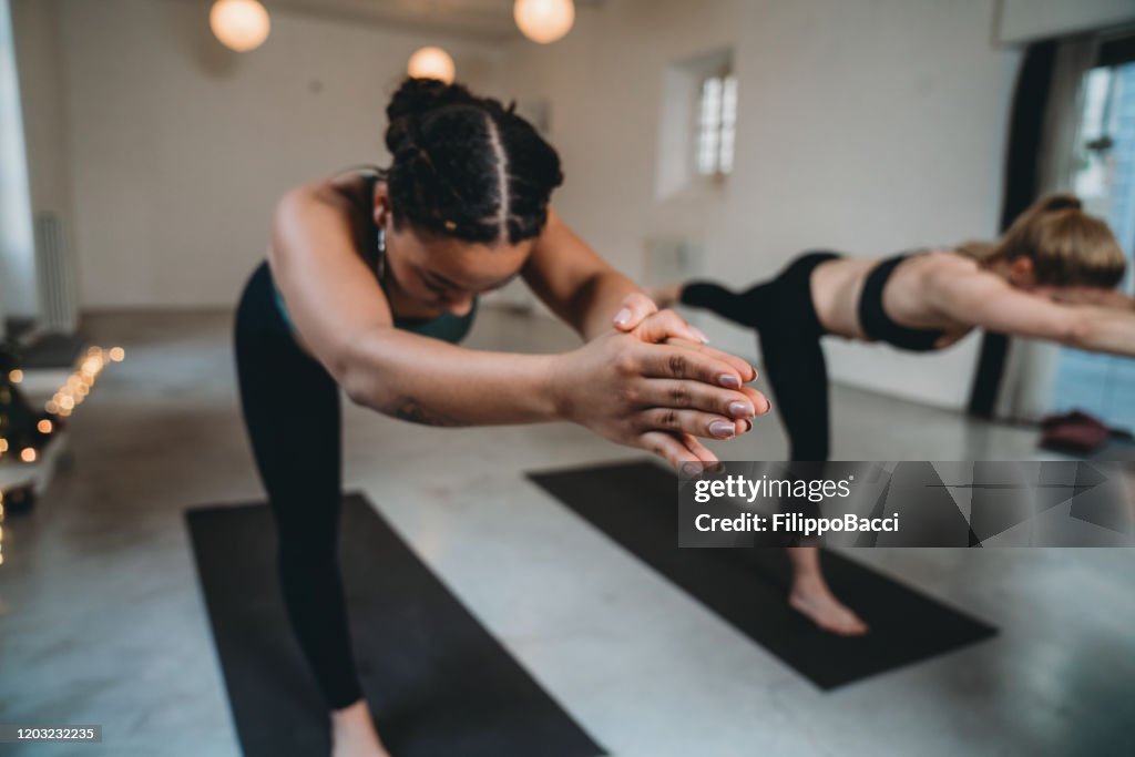 Young adult women together in warrior three pose at the yoga studio