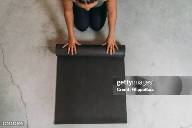 vue d'angle élevé d'une jeune femme adulte fermant un tapis de yoga - tapis de sol photos et images de collection