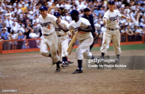 Duke Snider of the Brooklyn Dodgers is congratulated by his teammates Jackie Robinson and Don Hoak after hitting a homerun during an MLB game against...