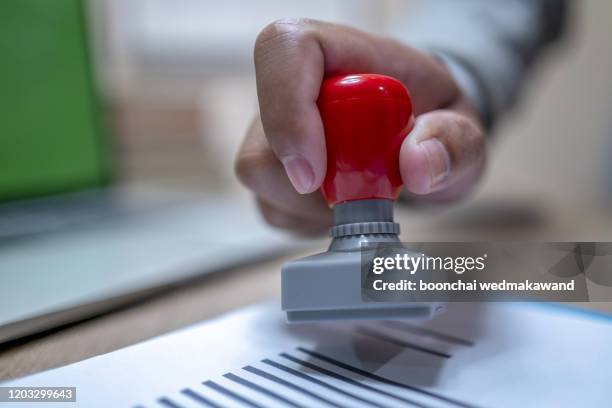 close-up of a person's hand stamping with approved stamp on document at desk - stenographie stock-fotos und bilder