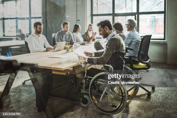 happy businessman in wheelchair reading documents during a meeting with his colleagues. - disabled accessibility stock pictures, royalty-free photos & images