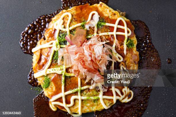 japanese okonomiyaki recipe. sprinkle sauce, mayonnaise, seaweed and bonito on okonomiyaki grilled on a hot plate. - okonomiyaki stock pictures, royalty-free photos & images