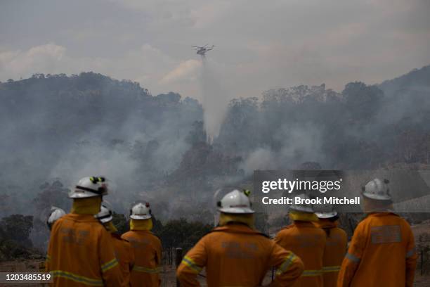 Firefighters watch as a helicopter water bombs a spot fire in the Orroral Valley on Boboyan Road. February 02, 2020 in Canberra, Australia. A total...