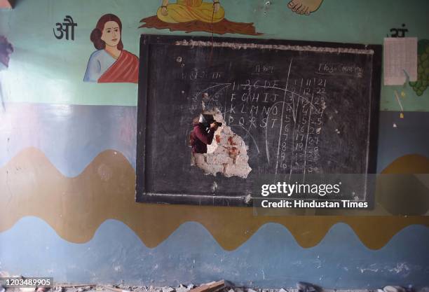 Photographer is seen through a damaged black board following violent clashes over the new citizenship law, at Shiv Vihar, on February 26, 2020 in New...