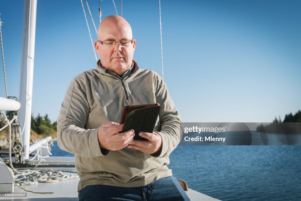 Senior Man Reading On Digital Tablet On His Sailboat