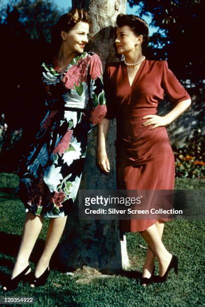 Full-length portrait of Joan Fontaine and her sister, Olivia de Havilland, both British actress, standing in conversation by a tree, circa 1945.